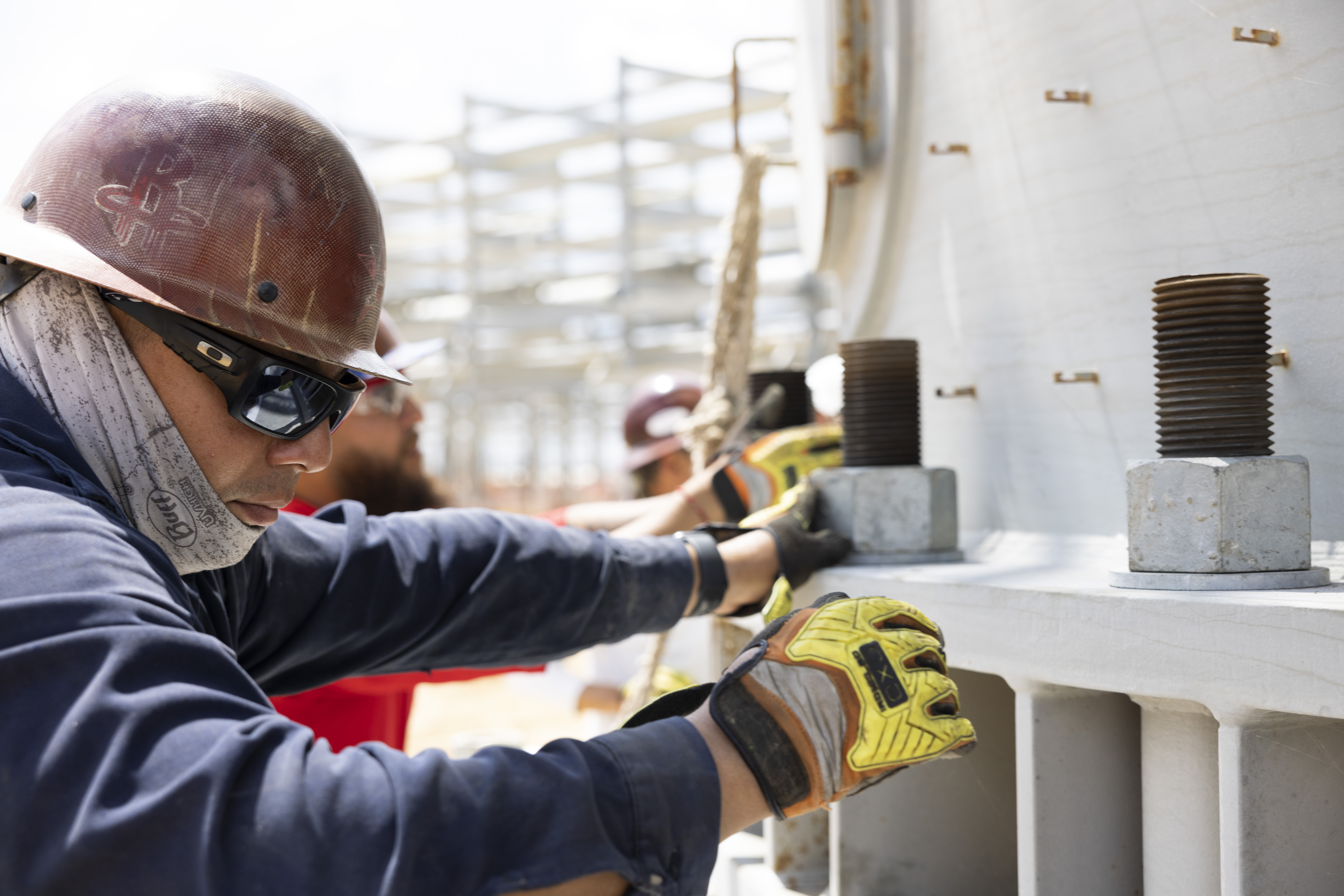 Construction worker tightening the bolt at the base of a large tower.